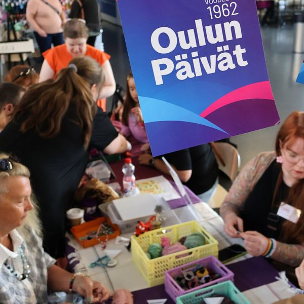 Kävijöitä neulomassa yhdessä pöytien ääressä tapahtuma-alueella